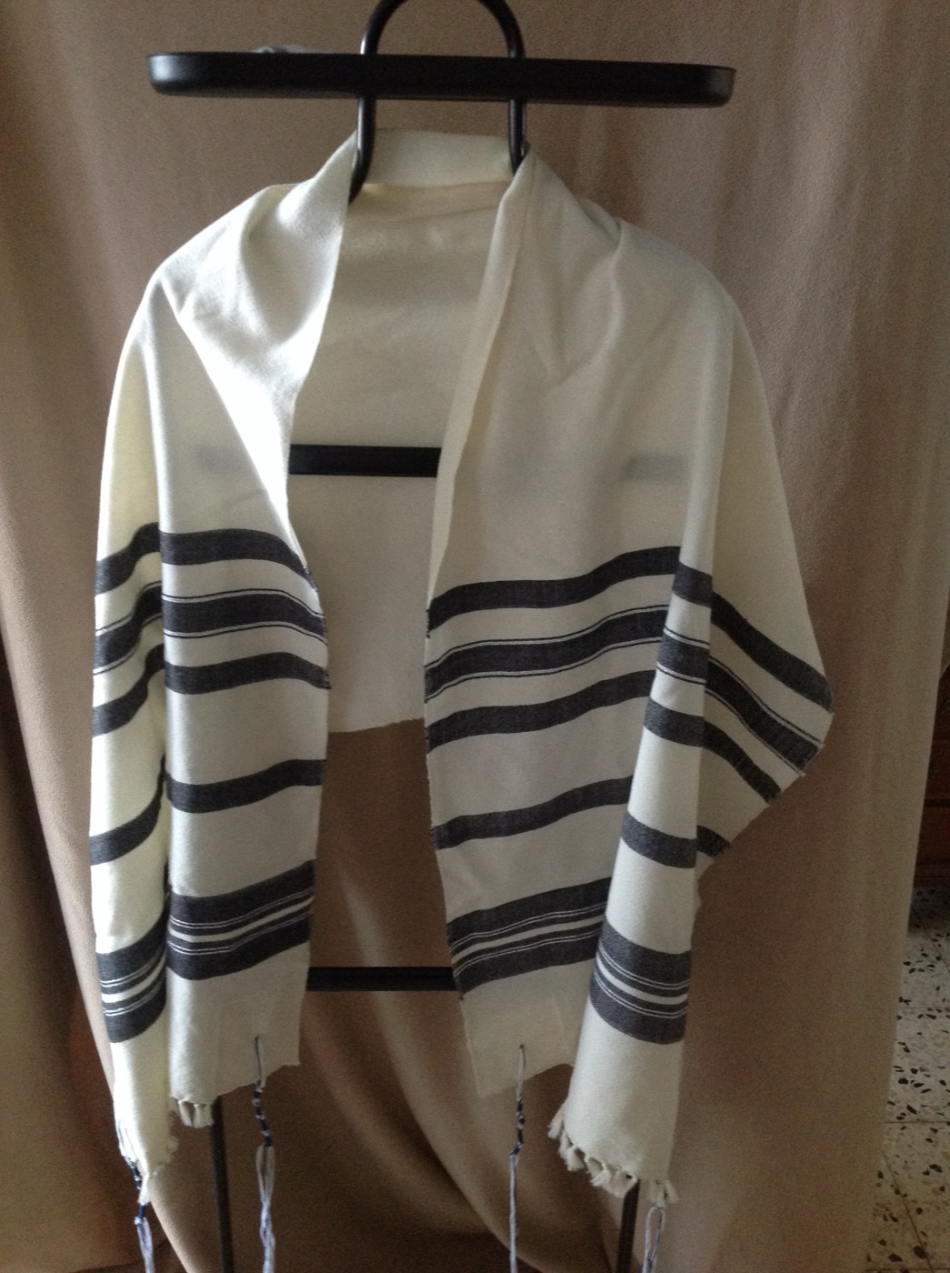 Hand-woven wool tallit with black stripes on a display stand