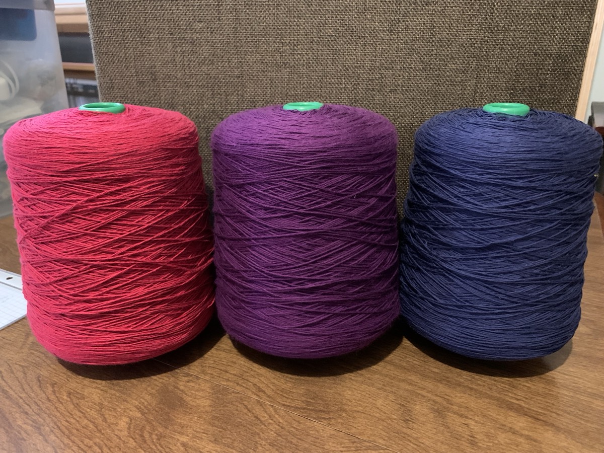 Cones of crimson, purple, and navy wool yarn